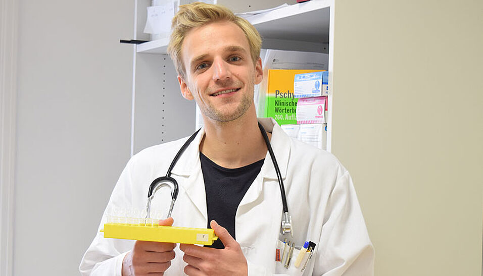 Andreas Goreis mit Arztkittel und Stethoskop und medizinischen Hilfsmitteln.