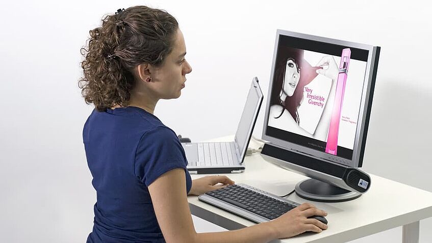 Frau sitzt vor einem Computer-Bildschirm und einem stationären Eyetracker