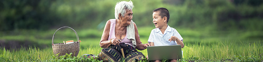 Eine alte Frau sitzt im Freien gemeinsam mit einem Buben vor einem Laptop.